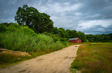 Dramatic cloudscape over the dirt road and a farmhouse in the wooded meadow