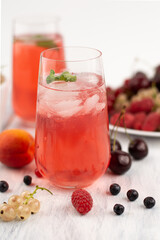 Blurred image of a fruit drink in a glass with ice on the background of a plate with fruit.
