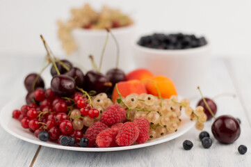 Blurred image of white plates with raspberries, currants, cherries, apricots, blueberries. Proper nutrition.