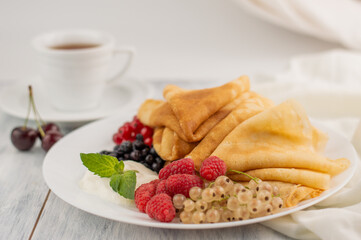 Blurred image of pancakes with fruit on white plate, a cup of tea on a light table.