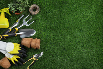 Flat lay composition with gardening tools and plant on green grass, space for text