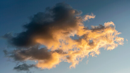 blue sky with a large cumulus cloud illuminated by the evening setting sun as a natural background