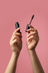 Woman holding mascara for eyelashes on dusty rose background, closeup