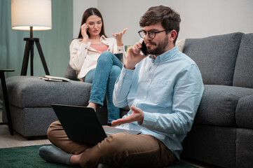 A man and a woman from a remote home office are having intense phone conversations from the home office, sitting on and next to the couch during lockdown