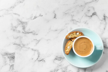 Tasty cantucci and cup of aromatic coffee on white marble table, top view with space for text....