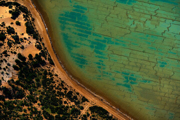 Abstract aerial view of blue-green water in shifting red deposition of sediment gradually moving through alluvial plains of Francois Peron National Park in Western Australia.