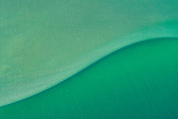 Abstract aerial view of blue-green water in shifting red deposition of sediment gradually moving through alluvial plains of Francois Peron National Park in Western Australia.