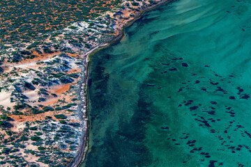 Abstract aerial view of blue-green water in shifting red deposition of sediment gradually moving through alluvial plains of Francois Peron National Park in Western Australia.