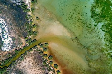 Abstract aerial view of blue-green water in shifting red deposition of sediment gradually moving through alluvial plains of Francois Peron National Park in Western Australia.