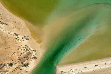 Abstract aerial view of blue-green water in shifting red deposition of sediment gradually moving through alluvial plains of Francois Peron National Park in Western Australia.