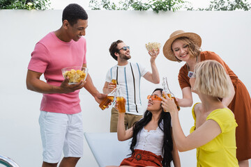 multiethnic friends smiling during summer party with beer and snacks