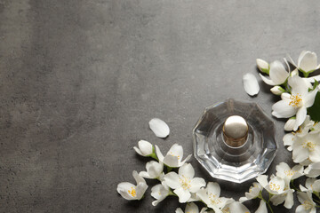 Bottle of luxury perfume and fresh jasmine flowers on grey table, flat lay. Space for text