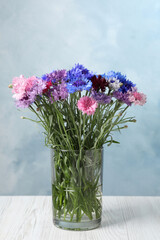 Bouquet of beautiful cornflowers in glass vase on white wooden table