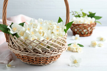 Fototapeta na wymiar Beautiful jasmine flowers in wicker basket on white wooden table