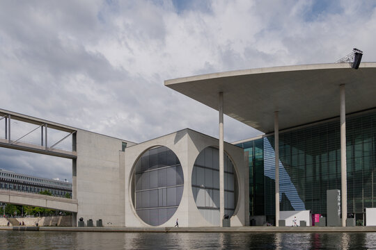 Outdoor exterior view of Marie-Elisabeth-Lüders-Haus, Federal government office, with rough concrete facade and big circle hole, along Spree River and pedestrian bridge in Berlin, Germany.