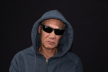 Naklejka na ściany i meble Older man wearing a dark hoodie and shades against a black background