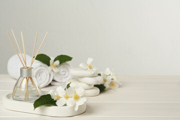 Fototapeta na wymiar Air reed freshener and beautiful jasmine flowers on white wooden table, space for text