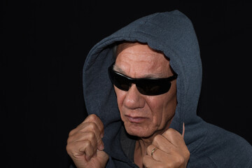 Older man wearing a dark hoodie and shades against a black background