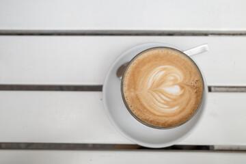Selective focus, heart  latte art and flat white coffee cup on the outdoor white wooden table.