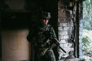 Military man with assault rifle standing inside building, he is ready for combat