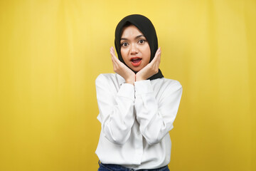 Beautiful young asian muslim woman shocked, surprised, wow expression, with hand holding cheek facing camera isolated on yellow background