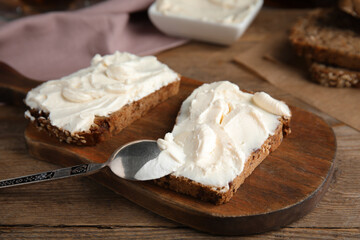 Bread with cream cheese on wooden table, closeup