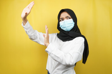 Muslim woman wearing medical mask with hand rejecting something, hand stopping something, hand disliking something, isolated on yellow background