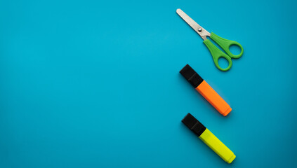 Scissors and colored markers isolated on a blue background. School supplies. Education concept. Copy space.