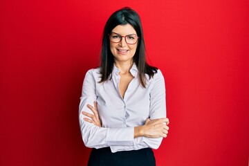Young hispanic woman wearing business shirt and glasses happy face smiling with crossed arms...