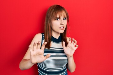 Redhead young woman wearing casual t shirt disgusted expression, displeased and fearful doing disgust face because aversion reaction. with hands raised