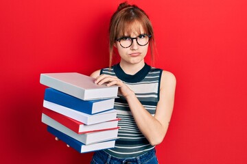 Redhead young woman holding a pile of books skeptic and nervous, frowning upset because of problem. negative person.