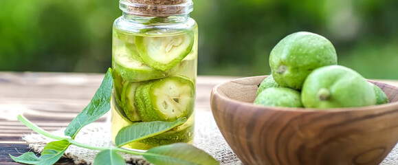 Smoothy unripe green walnuts and tincture of nuts in a transparent jar with a cork lid on an old vintage table. Leaves on branch of nut. Collect ingredients for tincture of nuts.
