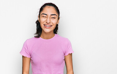 Fototapeta premium Hispanic teenager girl with dental braces wearing casual clothes winking looking at the camera with sexy expression, cheerful and happy face.