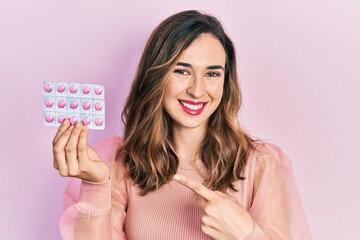 Young hispanic girl holding pills smiling happy pointing with hand and finger
