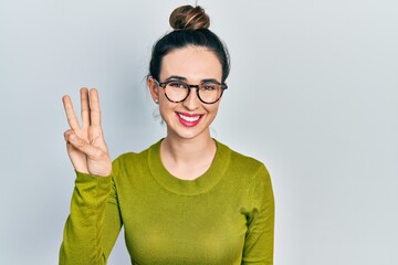 Young hispanic girl wearing casual clothes and glasses showing and pointing up with fingers number three while smiling confident and happy.