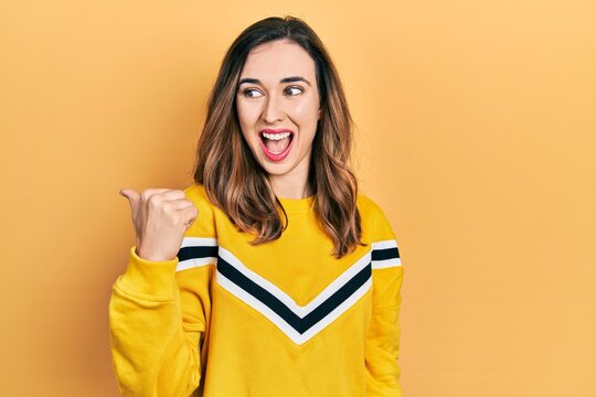 Young hispanic girl wearing casual clothes smiling with happy face looking and pointing to the side with thumb up.