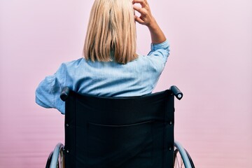 Beautiful blonde woman sitting on wheelchair backwards thinking about doubt with hand on head