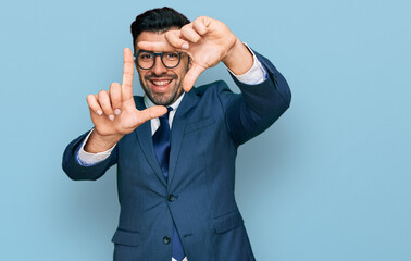 Hispanic man with beard wearing business suit and tie smiling making frame with hands and fingers...