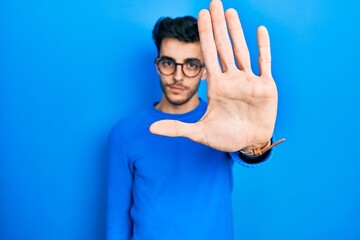 Naklejka premium Young hispanic man wearing casual clothes and glasses doing stop sing with palm of the hand. warning expression with negative and serious gesture on the face.