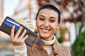 Beautiful hispanic woman with short hair smiling happy outdoors holding wallet with norwegian...