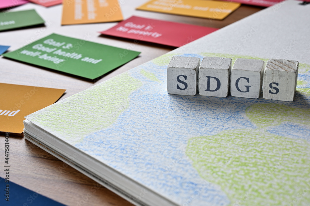 Poster there is a cube stamped with the letters of the sdgs on top of a sketchbook with a picture of the ea