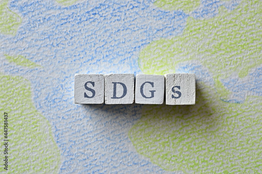 Poster there is a cube stamped with the letters of the sdgs on top of a sketchbook with a picture of the ea