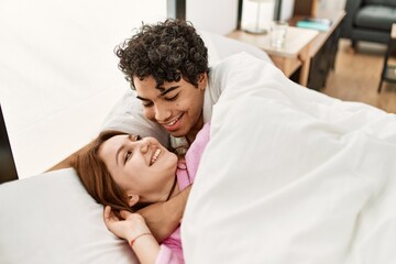 Young couple smiling happy and hugging lying on the bed at bedroom.