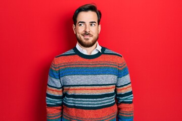 Handsome caucasian man with beard wearing elegant wool winter sweater smiling looking to the side and staring away thinking.