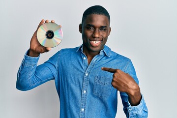 Young african american man holding compact disc pointing finger to one self smiling happy and proud