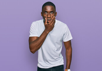 Young african american man wearing casual white t shirt looking fascinated with disbelief, surprise and amazed expression with hands on chin