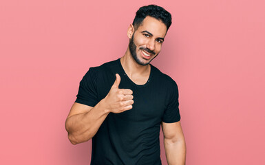 Hispanic man with beard wearing casual black t shirt doing happy thumbs up gesture with hand. approving expression looking at the camera showing success.