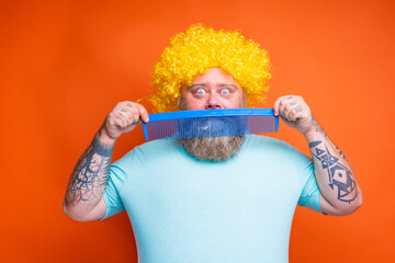 Fat amazed man with beard, tattoos and sunglasses combs himself with a giant comb