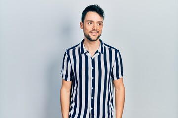 Fototapeta premium Young hispanic man wearing casual clothes looking away to side with smile on face, natural expression. laughing confident.