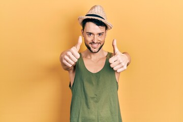 Young hispanic man wearing summer hat approving doing positive gesture with hand, thumbs up smiling...